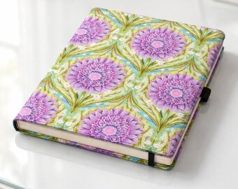 May include: A closed notebook with a floral pattern featuring large purple flowers with pink centers on a light green and blue background. The notebook has a black elastic band closure and is on a white surface.