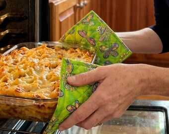 May include: A person using green quilted oven mitts with a butterfly and floral pattern to remove a glass baking dish of pasta from an oven. The mitts are lime green with a quilted design.