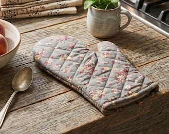 May include: Gray quilted oven mitt with a floral pattern in pink, yellow, and white. The mitt is on a wooden surface, next to a spoon, a bowl of peaches, and a mug with mint.