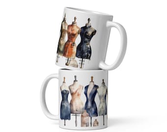 May include: Two white ceramic mugs stacked on top of each other. Each mug features a watercolor design of dressmaker mannequins in various colors. The top mug shows three mannequins, and the bottom mug shows five.