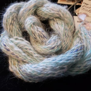 May include: A skein of yarn in shades of white, blue, and green with a subtle shimmer. The yarn is soft and fluffy, and it is perfect for knitting or crocheting.