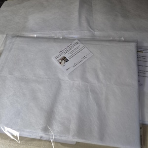 May include: A package of white fiber art supplies, including a sheet of white paper and a business card. The business card has the text "Plum Crazy Fiber Art" and contact information. The paper is in a clear plastic bag.
