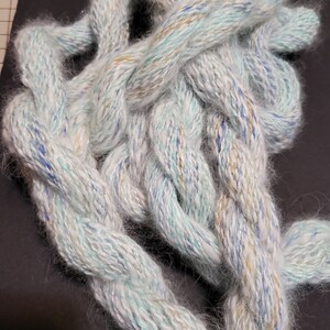 May include: A close-up of a white, blue, and gold yarn with a fuzzy texture. The yarn is twisted and knotted together.