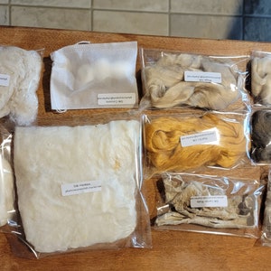 May include: A collection of silk fibre samples in clear plastic bags. The fibres are in various colours, including white, beige, gold, and grey. Some bags are labelled with text such as "Silk Hankies" and "Mulberry Silk". The fibres appear soft and fluffy.