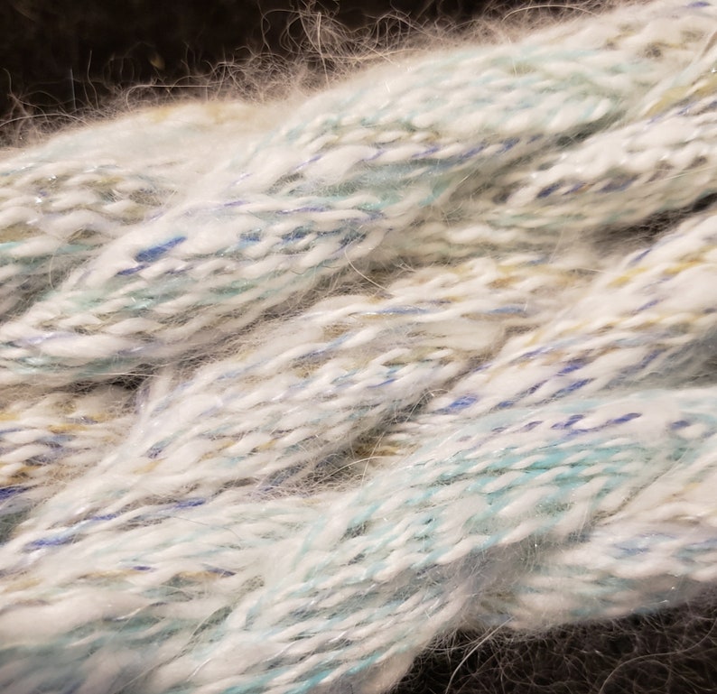 May include: Close-up of a white, blue, and beige yarn with a fuzzy texture. The yarn is twisted and piled together.