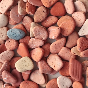 May include: A collection of small, smooth, red, orange, and brown stones. The stones have a rough, textured surface and are various shapes and sizes.