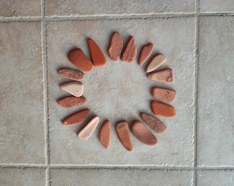 May include: A circle of small, flat, terracotta-colored stones arranged in a sunburst pattern on a light beige tiled floor.