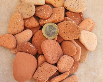 May include: A pile of small, reddish-brown, textured stones. A single euro coin is in the center of the pile for scale.