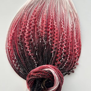 May include: A bundle of ombre braiding hair in black, red, and white. The hair is arranged in a fan shape with the ends tied together.