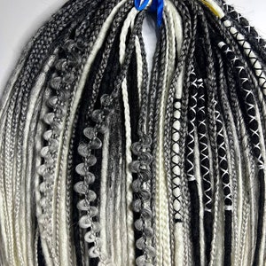 Könnte beinhalten: Ein Bündel schwarzer, weißer und grauer synthetischer Dreadlocks mit verschiedenen Texturen, darunter geflochtene, gehäkelte und gerade Strähnen. Die Dreadlocks sind mit einem blau-gelben Band zusammengebunden.