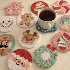 May include: A collection of Christmas-themed coasters with various designs, including a snowman, gingerbread man, Santa Claus, and a reindeer. The coasters are round and made of a textured material, with a cup of tea in the center.