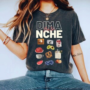 May include: A dark gray t-shirt with the text "Dima for Niche" printed in white. The shirt features a variety of colorful illustrations of food items, including a waffle, avocado, pretzel, and a cup of coffee.