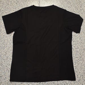 May include: A plain black short-sleeved t-shirt. The shirt has a V-neck and is made of a lightweight, possibly athletic material. The back of the shirt is visible, showing seams and a simple design.