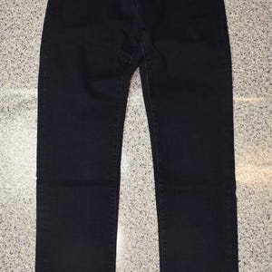 May include: Dark blue denim jeans with a classic five-pocket design. The jeans have a straight leg cut and a button and zipper closure. A small logo is visible on the front pocket. The jeans are made of a durable denim material.