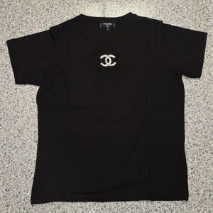 May include: Black short-sleeved t-shirt with a sparkling double-C logo on the chest. The shirt has a crew neck and the brand name is visible on the collar.