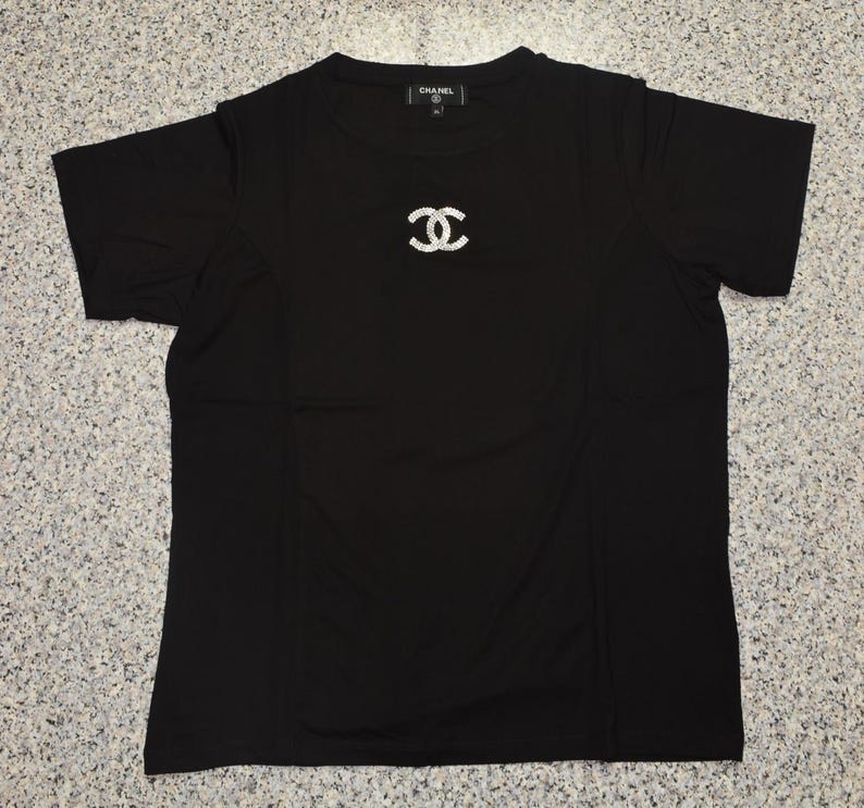 May include: Black short-sleeved t-shirt with a sparkling double-C logo on the chest. The shirt has a crew neck and the brand name is visible on the collar.