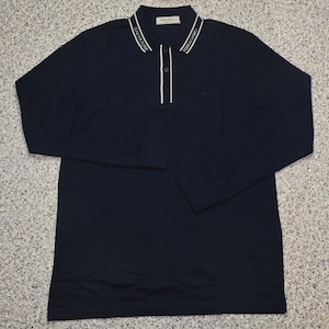 May include: A navy blue long-sleeved polo shirt with a white-trimmed collar. The collar features the brand name in white lettering. The shirt has a three-button placket and a small logo near the chest.