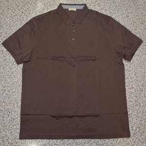May include: A short-sleeved, solid brown polo shirt with a collared neckline and three buttons. The shirt has a small logo on the chest and shoulder detailing. The fabric appears to be a lightweight material.