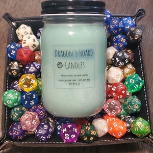 Może przedstawiać: Szklany słoik z tealową świecą, z czarną pokrywką i białą etykietą z napisem "Dragon's Hoard Candles". Etykieta zawiera r&oacute;wnież tekst "Mystery D20 in each candle", "40 Hour Burn Time | 100% Soy Wax" i "Net Wt 8 oz". Słoik ze świecą jest otoczony kolorowymi kostkami do gry.
