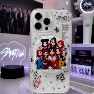 Op de afbeelding: Een doorzichtig telefoonhoesje met een ronde pop-out grip versierd met acht stripfiguren en de tekst K-POP. Het hoesje is bedrukt met zwarte stermotieven, het Stray Kids-logo en een lijst met namen waaronder Bang Chan.