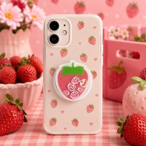 Op de afbeelding: Een doorzichtig telefoonhoesje met een herhalend patroon van kleine rode aardbeien en kleine roze hartjes. In het midden is een ronde, aardbeivormige telefoonhouder bevestigd met miniatuurbedeltjes van melkpakjes en aardbeien.