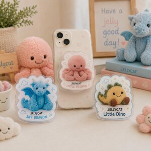 Puede incluir: Una funda transparente para smartphone con un agarre Jellycat Little Octopus. Dos soportes acrílicos se muestran delante, uno con un Sky Dragon azul con el texto Jellycat Sky Dragon, y el otro un Little Dino amarillo con Jellycat Little Dino.