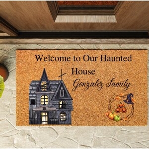 Peut inclure: Un paillasson rectangulaire avec le texte "Welcome to Our Haunted House Gonzalez Family". Il présente une illustration de maison hantée, des citrouilles et un chapeau de sorcière, parfait pour Halloween.
