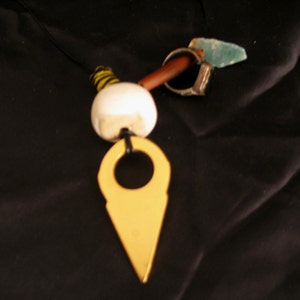 May include: A necklace with a white ceramic bead, a gold-colored pendant shaped like a pointed arrow, and a brown and green stone.