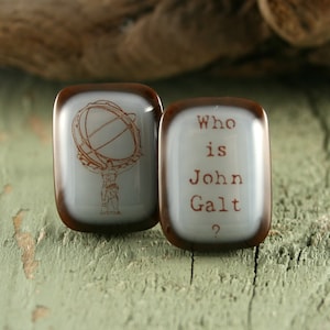 Pode incluir: Dois pequenos azulejos quadrados de vidro com bordas marrons. O azulejo à esquerda tem um desenho de uma pessoa segurando um globo. O azulejo à direita tem o texto "Who is John Galt?" em letras marrons.