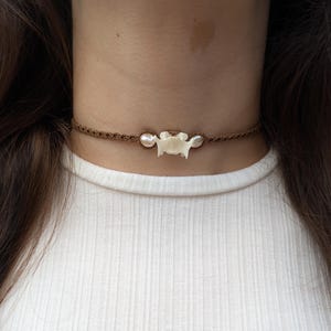 May include: A brown cord choker necklace with a white bone pendant and two white pearl beads.