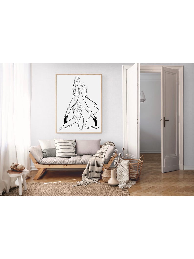 May include: A framed black and white line art print depicting two figures in an embrace. The artwork hangs above a wooden sofa with pillows and a striped blanket. The room has a neutral color palette with natural textures.