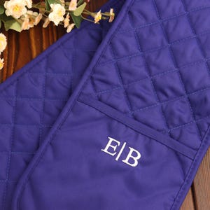 May include: A double-sided quilted oven glove in a deep royal purple colour. The glove features a diamond-stitched pattern across the surface and includes a white embroidered monogram with the letters E and B separated by a vertical line.