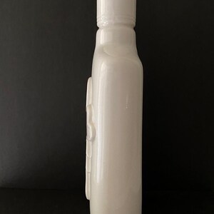 May include: A white ceramic bottle with a smooth, glossy finish. The bottle has a simple, elegant design with a rounded base and a slightly flared top.