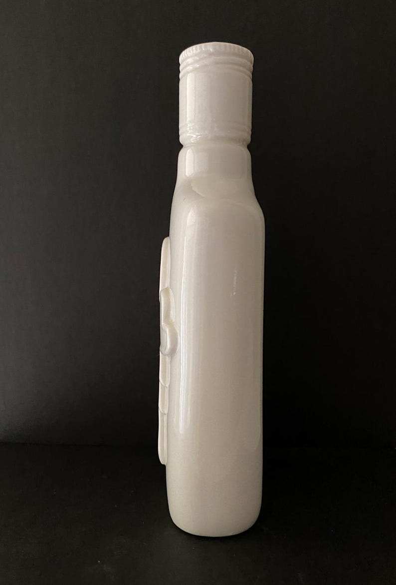 May include: A white ceramic bottle with a smooth, glossy finish. The bottle has a simple, elegant design with a rounded base and a slightly flared top.
