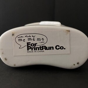 May include: White plastic container with a black label that reads "www.Made by me meme me.com For PrintRun Co. Made in China"