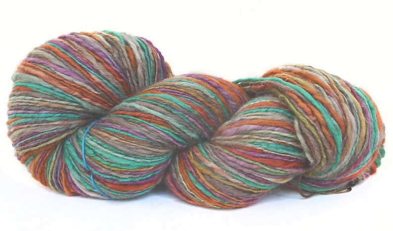 May include: A skein of yarn with a mix of colors, including teal, orange, brown, and purple. The yarn is made of natural fibers and has a rustic, hand-spun look.