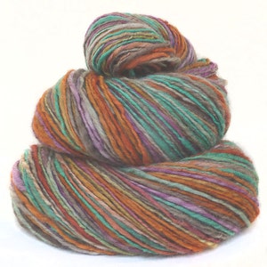 May include: A skein of yarn in a multi-colored pattern of orange, teal, purple, and gray. The yarn is wound into a ball and stacked on top of itself.