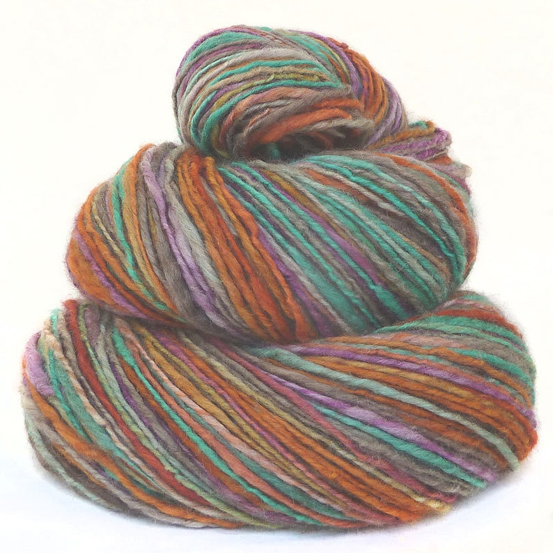 May include: A skein of yarn in a multi-colored pattern of orange, teal, purple, and gray. The yarn is wound into a ball and stacked on top of itself.