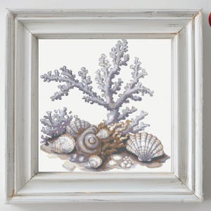 Könnte beinhalten: Ein Kreuzstichmuster mit einem violetten Korallenast und einer Ansammlung von Muscheln in Weiß- und Brauntönen.