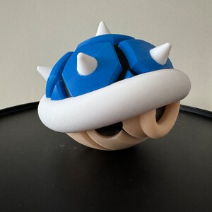 Könnte beinhalten: Eine blaue und weiße 3D-gedruckte Muschel mit Stacheln, die einem Charakter aus einem beliebten Videospiel ähnelt.