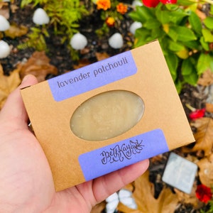 May include: A brown cardboard box with a lavender and patchouli scented soap bar inside. The box has a purple label with the text "lavender patchouli" and a smaller purple label with the text "Beth Kayla LLC".