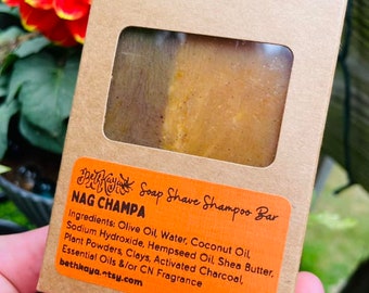 May include: A brown cardboard box with a window showing a bar of soap. The box has a label that reads "By Soap Shave Shampoo Bar" and "NAG CHAMPA". The label also lists the ingredients: Olive Oil, Water, Coconut Oil, Sodium Hydroxide, Hempseed Oil, Shea Butter, Plant Powders, Clays, Activated Charcoal, Essential Oils &/or CN Fragrance. The box also has the website address "bethkaya.etsy.com" and the weight "4.7oz".