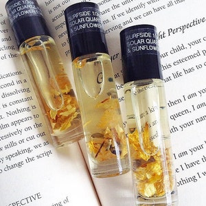 May include: Three glass bottles with black caps and labels that read "Surfside 1/3oz Solar Quartz & Sunflower". The bottles are filled with a clear liquid and contain dried yellow flower petals.
