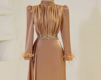 May include: A long-sleeved, gold satin dress with a high neck and a fitted bodice. The dress has a pleated skirt and a belt with embellishments. The sleeves have feather trim.