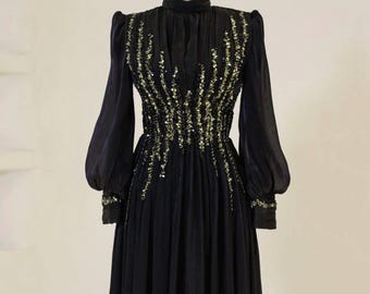 May include: A black long-sleeved dress with a high neckline and a fitted bodice. The dress is adorned with gold and black sequins in a geometric pattern.