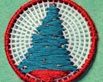 May include: A teal blue yarn Christmas tree stitched onto a white plastic canvas with a red yarn border.