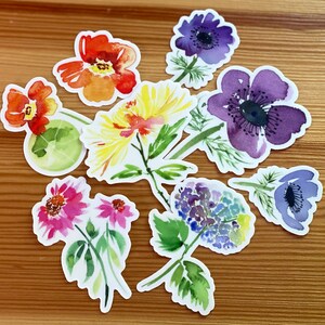 以下が含まれることがあります： 紫、青、黄、赤、ピンクの色合いの様々な花を描いた水彩の花のステッカー9枚セット。ジャーナル、プランナー、カード、その他のクラフトプロジェクトに遊び心を加えるのに最適です。