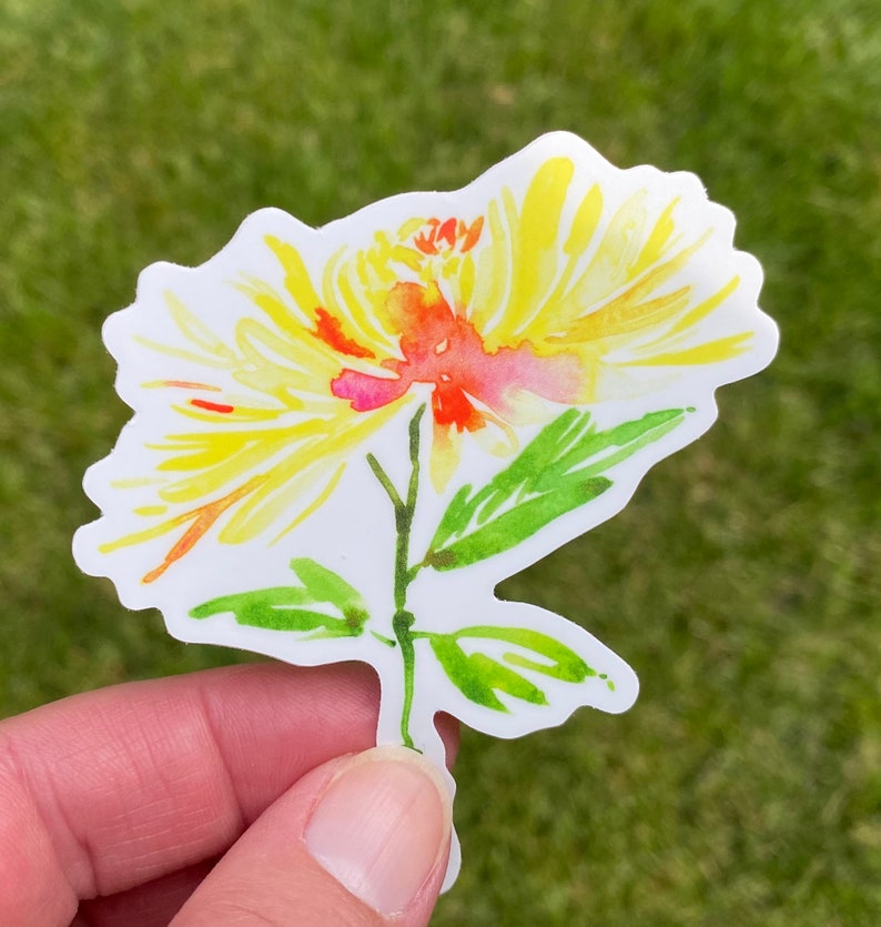 以下が含まれることがあります： 緑の葉が付いた黄色とオレンジの水彩画の花のステッカー。花は黄色い中心とオレンジとピンクの花びらを持っています。