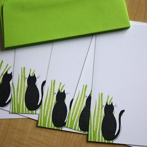 May include: Set of six blank note cards with a black cat silhouette design. Each card features a black cat sitting in green grass.