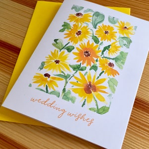 May include: A white card with a watercolor painting of yellow sunflowers and green leaves. The text "wedding wishes" is written in orange cursive at the bottom of the card.